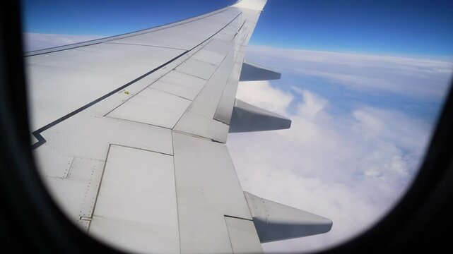 Airplane Wing Soaring High Above Clouds on Clear Day During Flight. Wing of plane extends out providing stunning view of fluffy clouds and blue sky
