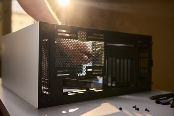 A man cleans a computer case with a vacuum in a bright room, stressing workspace tidiness