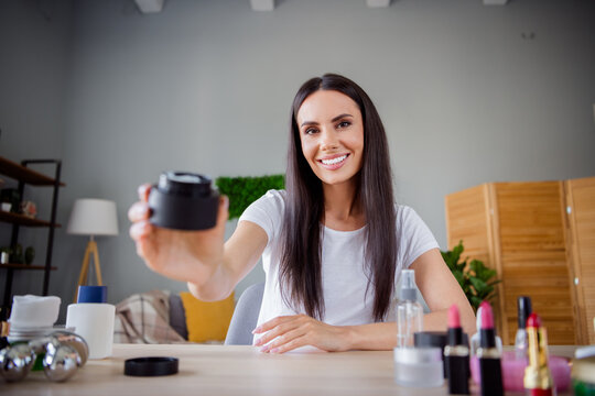 Photo of nice young girl show offer cream jar makeup artist recording cosmetics product review filming video home interior