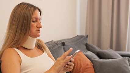 Woman sitting on sofa in cervical collar, feels support. Cervical collar is necessary for recovery after injury. Suitable for topics about health and problems with neck with cervical collar.