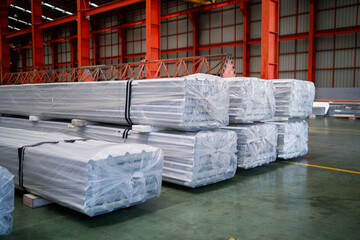 A warehouse full of steel pipes wrapped in plastic. The pipes are stacked in rows and are covered...