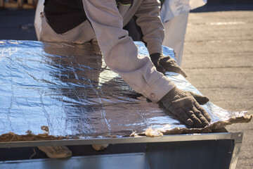 A person skillfully applying aluminum foil in a construction setting for insulation purposes
