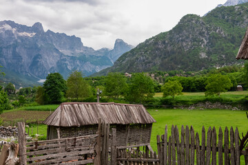 Rural wooden shed with thatched roof with view of mountain ridge massif Radohina in Albanian Alps (Accursed Mountains), Northern Albania. Scenic hiking trail to Theth. Wanderlust in alpine wilderness