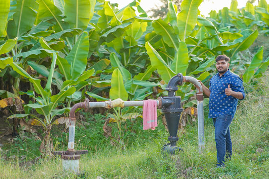 happy young indian farmer holding water pump