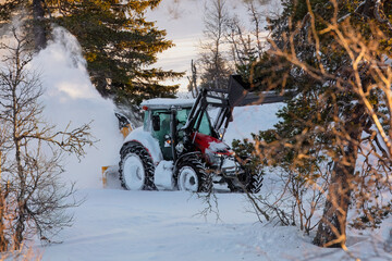 Snow plow tractor clearing snowy road throw the forest. Winter maintenance, rural road clearing.