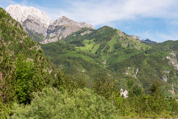 Naklejka premium Picturesque stone church of St. George nestled in idyllic village Theth, Northern Albania. Surrounded by pine tree forest and majestic mountain massif Prokletije, Albanian Alps (Accursed Mountains)