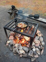 Cooking delicious meals over an open fire in a campsite using a metal grill and stone firepit surrounded by nature