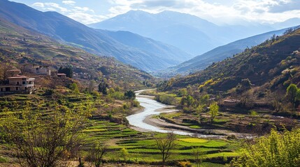 A winding river flows through a valley in the mountains, with green fields and trees on the slopes.