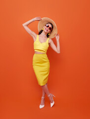 Happy young sexy woman slim body wear yellow swimsuit straw wide brim hat posing isolated on orange color background studio. Summer hotel pool sea rest sun tan concept