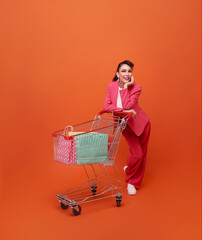 happy smiling woman shopper with trolley and shopping bags walking shopping promotion summer sale isolated on orange background.