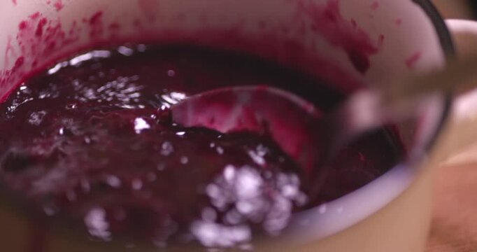Freshly made hot blueberry jam being stirred with a spoon in a detailed close-up video, showcasing the rich texture and vibrant color of the jam