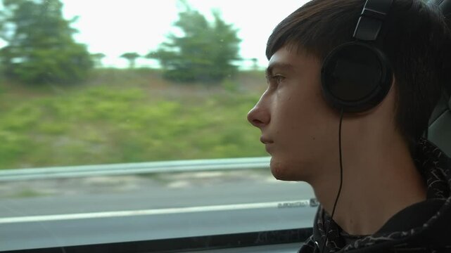 Sad thoughtful boy in headphones sits in bus, gazing out window with pensive expression. Teenager capturing quiet moment of introspection and daydreaming. Puberty, solo travel, vacations alone