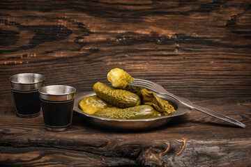 Delicious pickled cucumbers in a metal bowl with a fork on a wooden table.