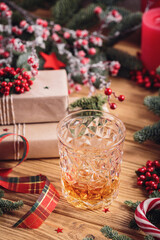 Glass of whiskey or bourbon with festive Christmas decoration on light wooden background. New Year, Christmas and winter holidays whiskey mood concept