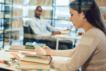 Pensive colleagues browsing smartphones in library