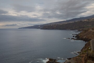Fototapeta premium Volcanic rocky coast with blue color of water in evening. Shore of Atlantic Ocean in Puerto de la Cruz. Travel concept. Amazing view of Tenerife island north coast. Gloomy weather