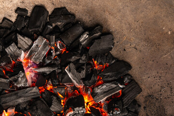 Hot coals with vibrant red and orange hues, emitting intense heat. Glowing pieces surrounded by dark ash, creating a rustic atmosphere