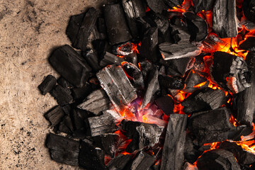 Hot coals with vibrant red and orange hues, emitting intense heat. Glowing pieces surrounded by dark ash, creating a rustic atmosphere