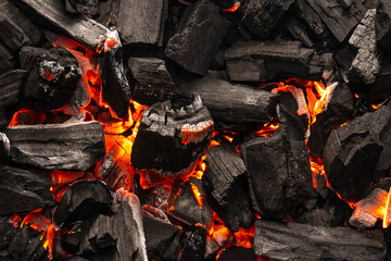 Hot coals with vibrant red and orange hues, emitting intense heat. Glowing pieces surrounded by dark ash, creating a rustic atmosphere