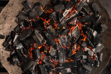 Hot coals with vibrant red and orange hues, emitting intense heat. Glowing pieces surrounded by dark ash, creating a rustic atmosphere