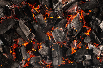 Hot coals with vibrant red and orange hues, emitting intense heat. Glowing pieces surrounded by dark ash, creating a rustic atmosphere