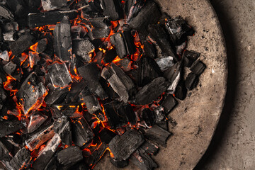 Hot coals with vibrant red and orange hues, emitting intense heat. Glowing pieces surrounded by dark ash, creating a rustic atmosphere