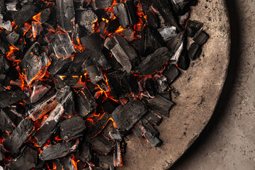 Hot coals with vibrant red and orange hues, emitting intense heat. Glowing pieces surrounded by dark ash, creating a rustic atmosphere