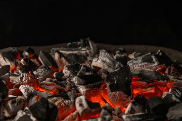 Hot coals with vibrant red and orange hues, emitting intense heat. Glowing pieces surrounded by dark ash, creating a rustic atmosphere