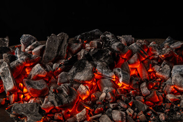 Hot coals with vibrant red and orange hues, emitting intense heat. Glowing pieces surrounded by dark ash, creating a rustic atmosphere