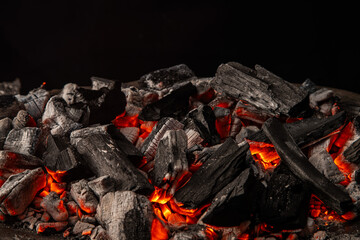 Hot coals with vibrant red and orange hues, emitting intense heat. Glowing pieces surrounded by dark ash, creating a rustic atmosphere