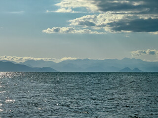 Serene lakeside scene with calm, shimmering surface of Skadar lake, Albania. Reflecting soft light of setting sun casting golden hue. Scenic view of Dinarc Alps mountains, Southern Montenegro. Summer