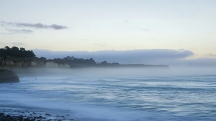 Obraz premium A misty dawn breaks over a rocky coastline, with the ocean stretching out in the distance.