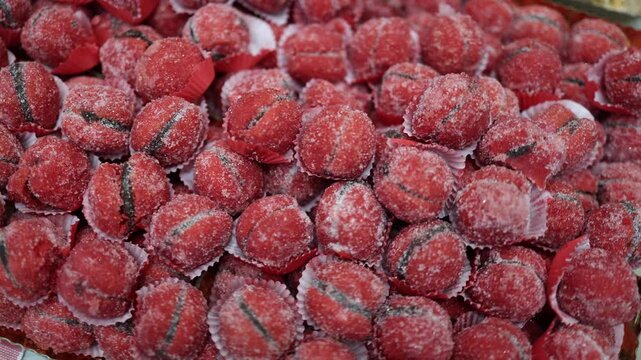 Bright red sugared candies with a dark filling, resembling mini peaches, beautifully arranged in paper cups. These vibrant treats add a festive touch, perfect for sweet tooth lovers and dessert displa