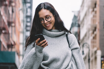 Cheerful young woman surfing on smartphone on street