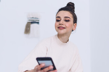 Young woman in home style wear sitting on bed and using devises