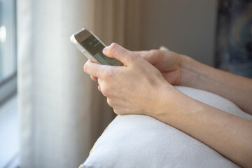 Close up of a young woman holding her smartphone in the comfort of her home, scrolling through social media, reading or shopping online.