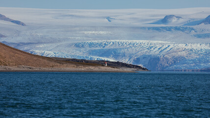 Nordenskiold Glacier in Svalbard with a distant coastal lighthouse under clear skies