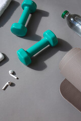 Sport or workout concept flat lay with blue dumbbells, yoga mat and white wireless headphones on the grey background. Copy space
