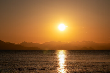 Breathtaking sunset over calm Skadar lake, Albania. Sun is setting behind Dinaric Alps mountains in Montenegro. Water reflects vibrant colors of sky creating shimmering path across the surface