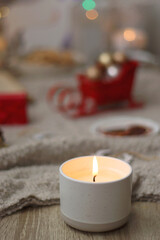 Various Christmas decorations, lit candles, cup of tea or coffee, cookies, books, presents and soft blanket on the table. Holiday hygge at home. Selective focus.