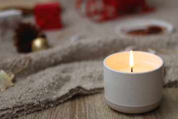 Various Christmas decorations, lit candles, cup of tea or coffee, cookies, books, presents and soft blanket on the table. Holiday hygge at home. Selective focus.
