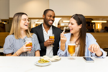 A group of 3 friends of different ethnicities have fun in a beautiful restaurant.Young people have fun while having an aperitif and drinking beer.Friends in a bar concept.