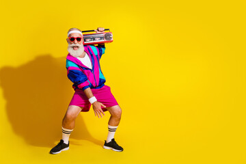 Full length photo banner of sportive cheerful old man dancing music boom box dressed stylish retro sportswear isolated on yellow background © deagreez