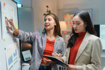 Two businesswomen having a discussion about a business strategy while looking at a whiteboard in an...