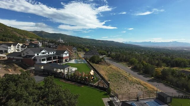 Drone flying on the hilly Bountiful city, showing houses, roads and lush greens on a sunny day