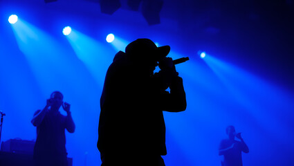 Silhouette of rap singer performing on stage. Bright blue background with hip hop artist performing on concert in night club