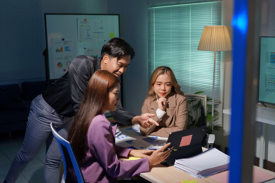 Group of asian businesspeople are having a late night work meeting in the office, using a tablet and going over paperwork