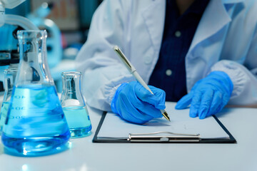 Fototapeta premium Scientist wearing blue gloves writing down experiment results on a clipboard in a laboratory