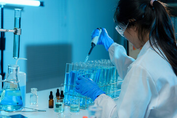 Scientist wearing a lab coat and safety glasses is carefully dropping liquid into a test tube using...
