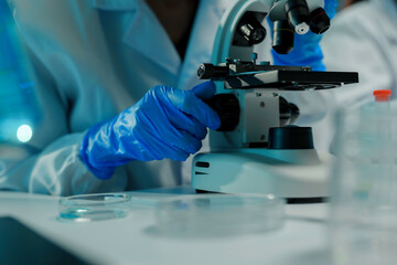 Scientist wearing blue gloves adjusting a microscope, conducting research in a laboratory setting